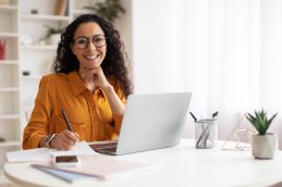 Uma mulher sentada em uma mesa de frente para um notebook, sorrindo após entender todas as principais siglas do glossário de empreendedorismo