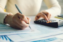 Mulher usando uma calculadora e anotando os resultados no papel para fazer as contas do Imposto de Renda 2023.