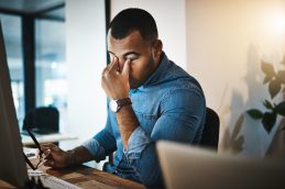 Um homem com as mãos nos olhos e uma expressão de estar sob estresse, representando que ele pode estar tendo um burnout