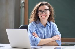 Uma mulher sentada em uma cadeira em frente a um computador, olhando para frente e sorrindo por saber os motivos para fazer um MBA em Gestão de Riscos e Compliance
