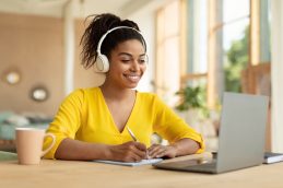 Uma mulher em frente ao computador sorrindo por estar aproveitando das vantagens de estudar online