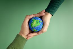 Duas pessoas dando as mãos, com uma miniatura de planeta terra no meio, representando o impacto positivo de profissionais que fizeram um curso ESG em empresas de todo o mundo
