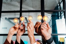 Cinco pessoas levantando lâmpadas acessas, representando o impacto da visão estratégica na elaboração de novas ideias
