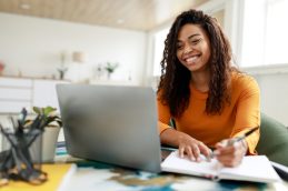 Uma mulher em frente ao computador, com um bloco de anotações, representando que ela é uma lifelong learner e iniciou um MBA